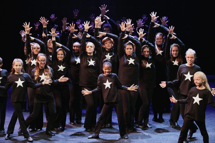 Large group of kids performing and dancing with jazz hands