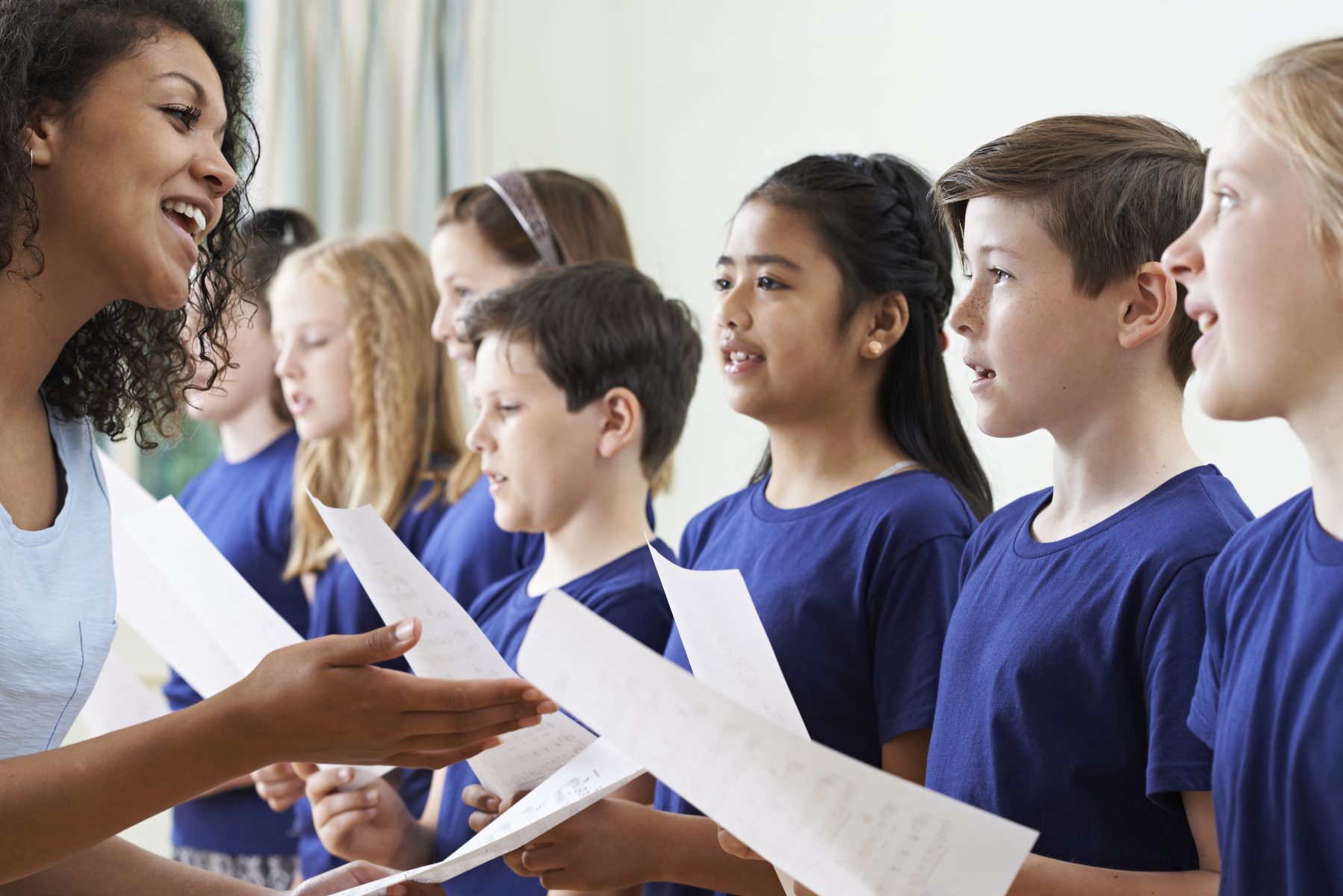Kids holding sheet music with teacher in choir class