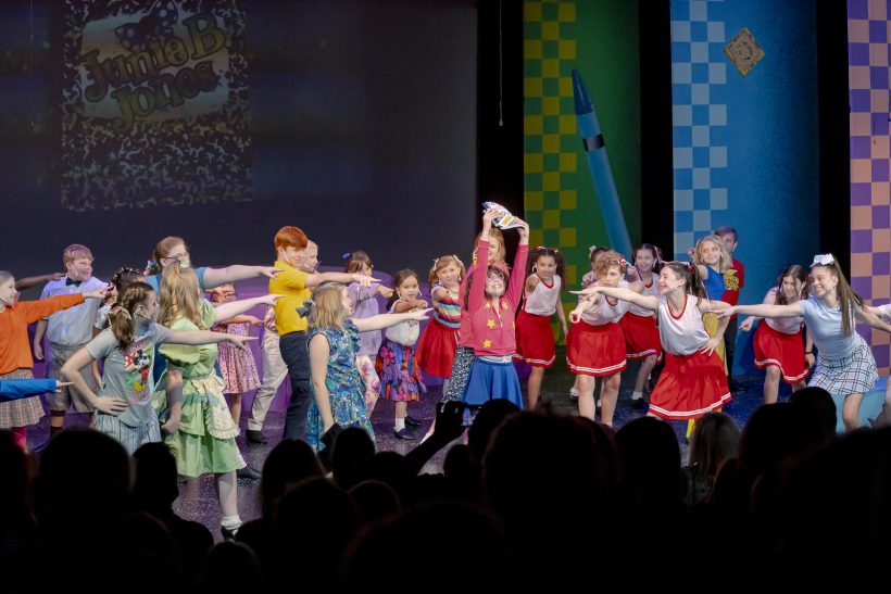 students pointing at girl in pink sweater holding book