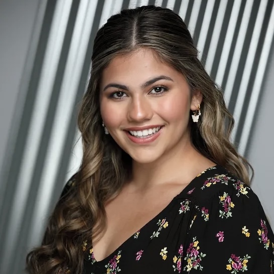 Young woman with brown hair and eyes in a floral shirt with a white and grey background