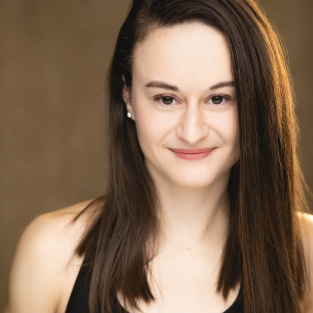 Woman with brown hair and eyes in a black tank top with a brown background