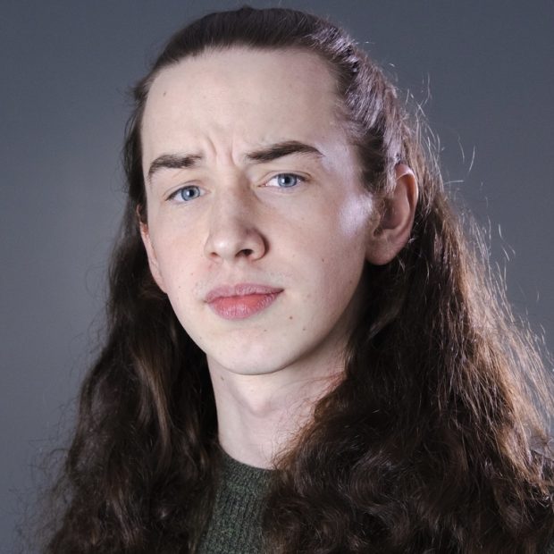 Young man in green sweater with long brown hair and blue eyes with grey background