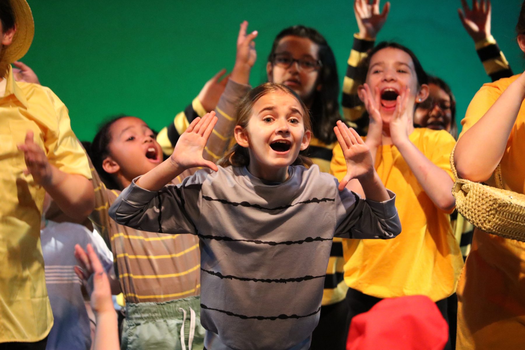 girl in gray sweatshirt singing with more kids behind her